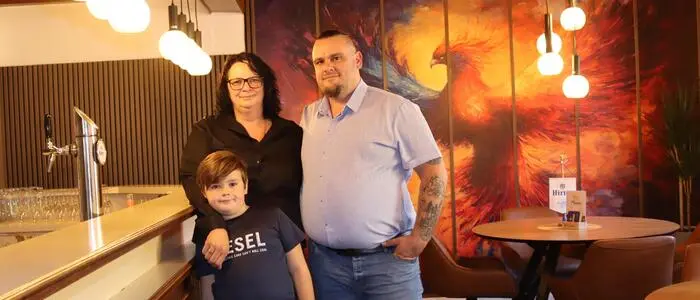 Eine Familie steht neben einer Bar in einem Restaurant und lächelt in die Kamera.
