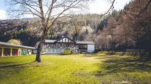 Ein Restaurant von oben, am dazugehörigen Parkplatz stehen mehrere Autos, im Hintergrund sind der Millstätter See und die Berge zu sehen