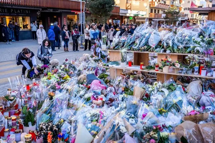People gather around a makeshift memorial to pay their respects by laying flowers, candles and messages near the Constellation bar, on January 4, 2026, in Crans-Montana in honour of the victims of the fire that ripped through the venue in the luxury Alpine ski resort on New Year's Eve. Authorities investigating the New Year's blaze in the Swiss resort of Crans-Montana have identified 24 of the 40 people killed, including 11 minors and six foreign nationals, police said on January 4, 2026. Also 119 were injured during the fire, most of them seriously, according to the latest toll. (Photo by MAXIME SCHMID / AFP)