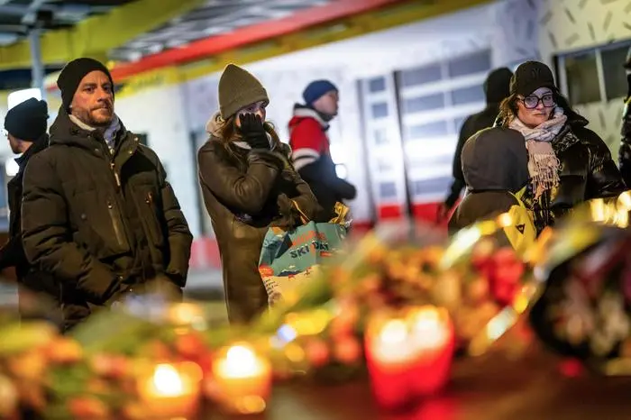 Mourners gather in front of flowers and candles laid near the site where a fire ripped through a crowded bar during New Year's Eve celebrations in the Alpine ski resort town of Crans-Montana on January 1, 2026. Several dozen people are presumed dead and around 100 injured after a fire ripped through a crowded bar in the luxury Swiss ski resort of Crans-Montana, Swiss police said on January 1, 2026. Police, firefighters and rescuers rushed to the popular resort, which is set to host the Ski World Cup from January 30, after the fire broke out in the early hours of New Year's Day. (Photo by MAXIME SCHMID / AFP)