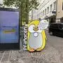 Neben einer digitalen Werbetafel in einer Fußgängerzone steht ein gelber Pinguin mit der Aufschrift „Pfandolin“