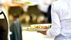 Eine Dame serviert zwei Teller an einen Tisch