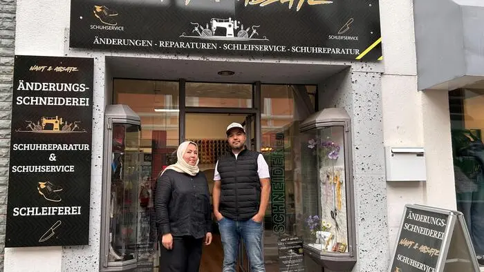 Eine Frau und ein Mann stehen vor einem Geschäft, das Änderungen und Schuhreparaturen anbietet