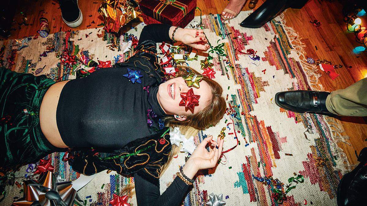 Laughing woman lying on floor with bows over eyes during holiday party with friends