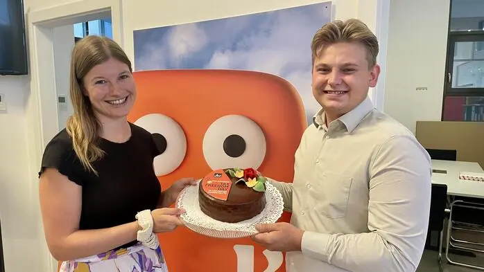 Sophie Anderwald und Tobias Vecsei mit einer Torte auf der die orange Fläche für jenen Zeitraum steht, in dem Menschen für die eigene Tasche arbeiten 