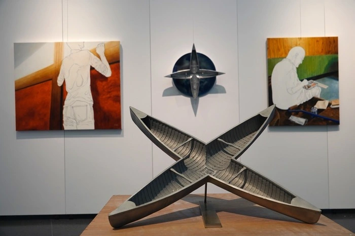 Skulptur "Kreuzfahrt III" mit zwei kreuzförmig ineinander gefügten Kanus, die eine Situation der Ausweglosigkeit symbolisieren und auch auf die Problematik der Flüchtlinge im Mittelmeer hinweisen, vor Werken, die Lackner in seiner selbst entwickelten Strichtechnik gestaltet hat.