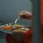 Close up of elderly prisoner in orange uniform sitting in prison cell, eating food. Criminal serves imprisonment term. Jail, detention center or correctional facility. Shooting through metal bars.