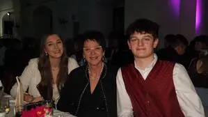 Zwei Frauen und ein Mann sitzen an einem Tisch im Ball-Outfit