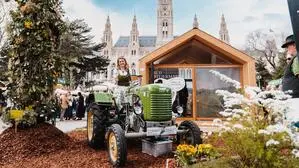 Auf dem Foto sieht man eine blonde Frau im Dirndl auf einem grünen Oldtimer-Traktor vor dem Wiener Rathaus | Auch heuer präsentieren sich wieder zahlreiche südweststeirische Betriebe am Wiener Rathausplatz