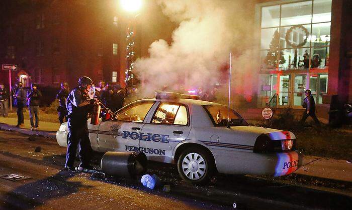 Ein Polizist versucht ein brennendes Polizeiauto zu löschen
