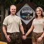 
Ein Mann und eine Frau in Lederhosen und T-Shart halten sich an der Hand. Zwischen ihnen das Logo des Lokals