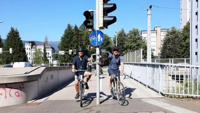 Zwei Radfahrer stehen an einer Ampel und halten sich an Griffen fest