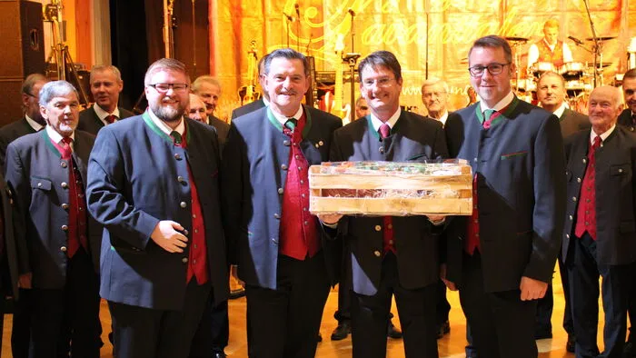 Chorleiter Lukas Joham, Obmann Josef Lobnig und Obmannstellvertreter Markus Liebhard übergaben Heinz Amschl (MGV St. Stefan i. Lav., 3. v. l.) einen Geschenkkorb als Dankeschön für ihren Auftritt.