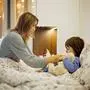 Cute sick child, boy, staying in bed, mom giving him medicine and checking for fever