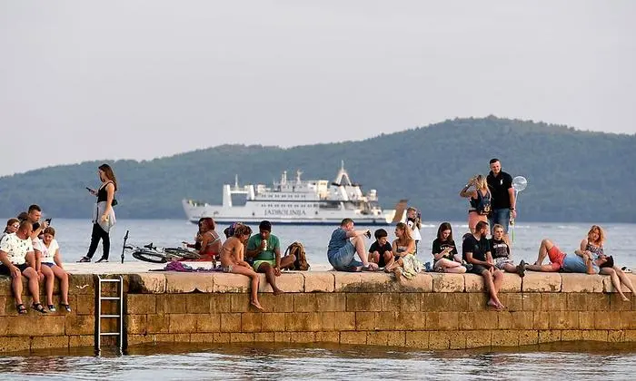 People sit or walk on a pier at sunset in Zadar, on the Adriatic coast on August 6, 2020. - A large number of tourists visited the Zadar Riviera, regardless of the novel coronavirus pandemic. Tourism is very important for Croatia, as almost 20% of GDP comes from it. (Photo by Denis LOVROVIC / AFP)