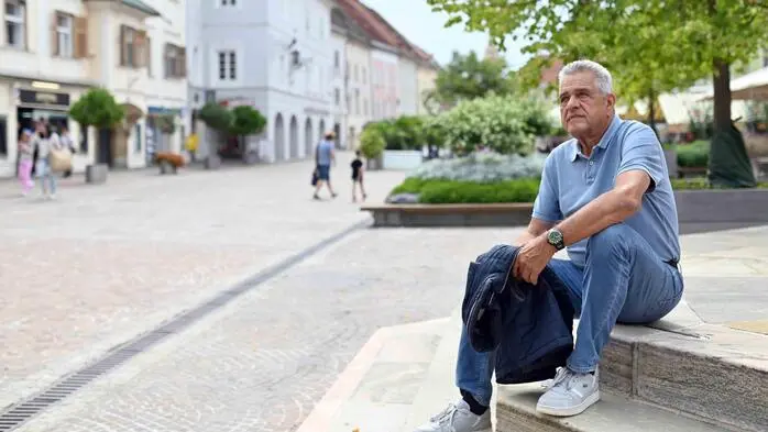 Ein Mann, Anfang 70, sitzt auf den Stufen auf dem Hauptplatz in der St. Veiter Innenstadt. Er blickt nachdenklich nach oben.