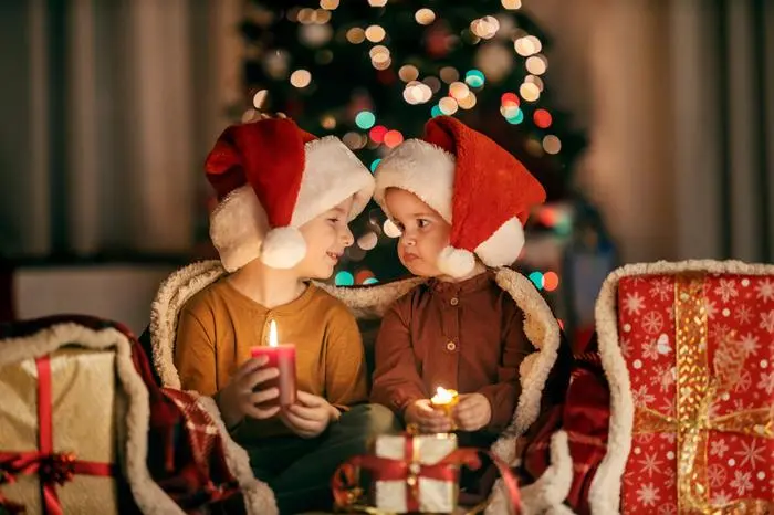 Jolly brother and sister sitting at home on christmas and new year's eve with candles in hands and looking at each other.