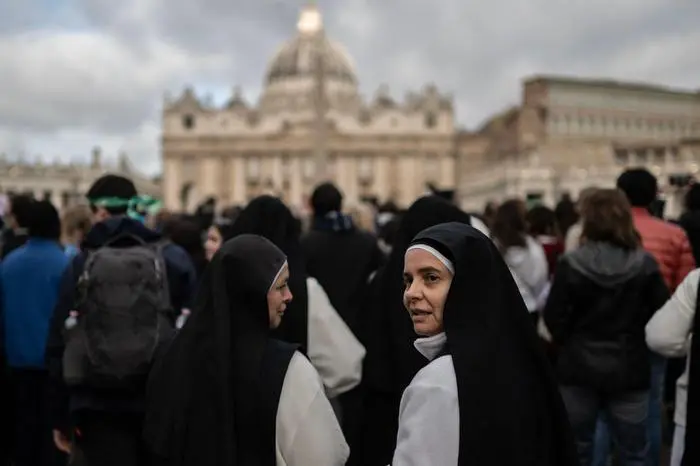 TOPSHOT - Nuns look on as they queue to enter the Vatican, with St Peter's Basilica in the background in Rome on April 25, 2025. The Vatican on April 25, 2025, said over 128,000 people have already paid their respects to Pope Francis, whose body is lying in state in St Peter's Basilica ahead of his funeral. (Photo by MARCO BERTORELLO / AFP)