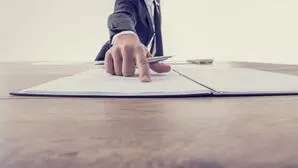 Ein Mann im Anzug (Kopf nicht im Bild) zeigt mit dem Zeigefinger auf einen Zettel, in der Hand hält er einen Stift