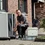 Zu sehen ist ein Installateur, der ein Außengerät einer Wärmepumpe installiert | Von Mai bis September ist Hochsaison für den Heizungstausch