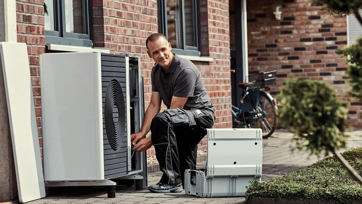 Zu sehen ist ein Installateur, der ein Außengerät einer Wärmepumpe installiert | Von Mai bis September ist Hochsaison für den Heizungstausch