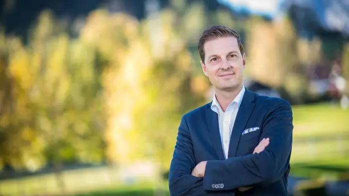 Das Bild zeigt Thomas Reingruber: helles Hemd, blaues Sakko, kurze, dunkle Haare, Arme verschränkt