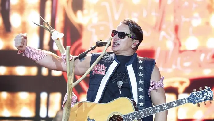 Andreas Gabalier singt in ein Mikrofon. Er trägt eine Sonnenbrille und hat eine Gitarre umgehängt.