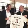Zwei Politiker halten ein T-Shirt in der Hand und schauen sich dabei gegenseitig an.
