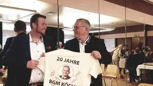 Zwei Politiker halten ein T-Shirt in der Hand und schauen sich dabei gegenseitig an.