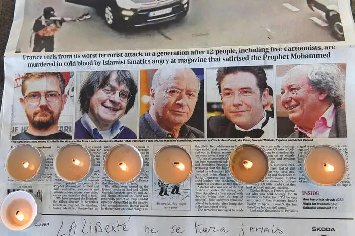 (FILES) Candles are placed on a newspaper bearing pictures from (L) of French satirical weekly Charlie Hebdo's editor and cartoonists Charb, Jean Cabut, aka Cabu, Georges Wolinski and Michel Renaud who were killed the day before in an attack by two armed gunmen on the offices of French satirical newspaper Charlie Hebdo, during a gathering in Marseille, on January 8, 2015. Ten years ago, the killings began on January 7 with an assault on the Charlie Hebdo satirical magazine in Paris that saw two brothers massacre 12 people including some of the country's best-known cartoonists, the killing of a policewoman and the storming of a Jewish supermarket on the eastern fringes of the capital which killed 4 local residents. (Photo by Anne-Christine POUJOULAT / AFP)