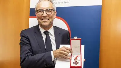 Ein Mann im dunklen Anzug und Brille hält eine Urkunde und eine Medaille in die Kamera