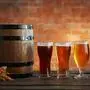 Glasses with different sorts of craft beer, wooden barrel and barley ears on brick wall background