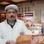 Ein Mann mit schwarzem Bart und weißem Kittel hält einen Leberkäse