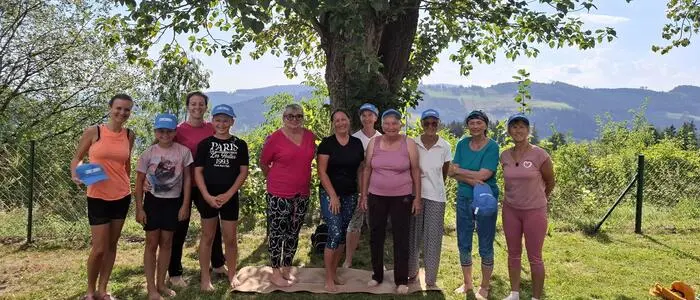 Mehrere Personen unterschiedlichen Alters stehen in sommerlicher Kleidung vor einem Baum