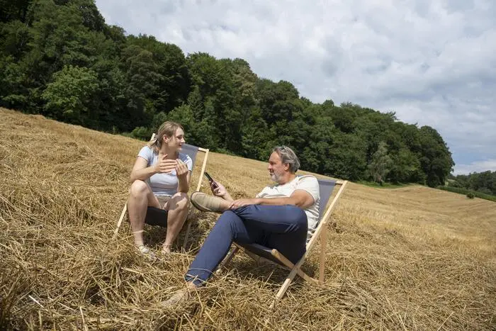Eine junge Frau und ein Mann sitzen in Liegenstühlen auf einem Acker im Stroh.
