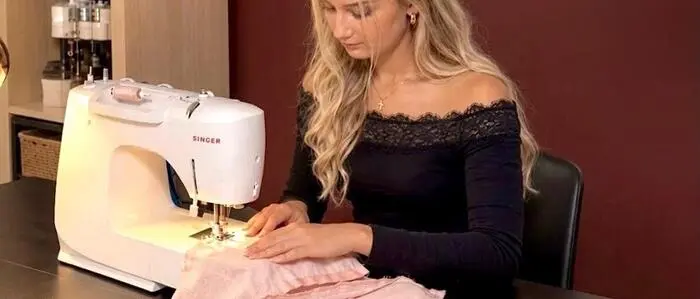 Eine junge Frau sitzt an einer Nähmaschine in ihrem Atelier und näht ein Kleidungsstück