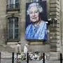 Pedestrians walk past a portrait of Queen Elizabeth II and flowers laid out at the British Embassy in Paris, September 9, 2022, a day after the Queen died at the age of 96. - Queen Elizabeth II, the longest-serving monarch in British history and an icon instantly recognisable to billions of people around the world, died at her Scottish Highland retreat on September 8. (Photo by Ludovic MARIN / AFP)
