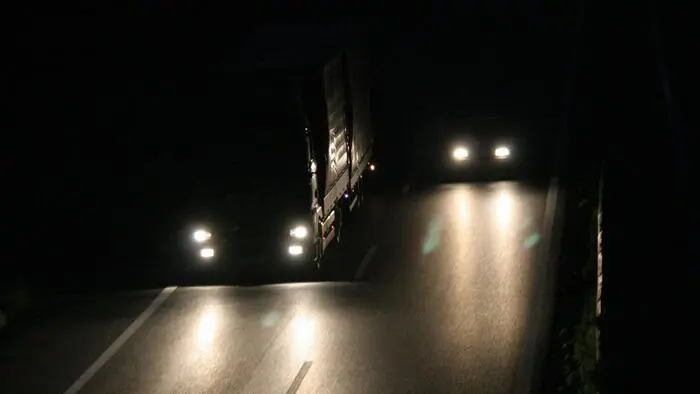 Das Bild zeigt einen LKW, der neben einem PKW bei Dunkelheit auf der Autobahn fährt