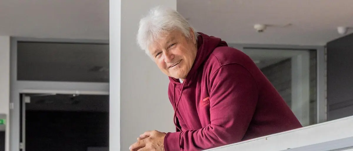 Ein Mann der sich auf eine Mauer lehnt. Darunter steht „Schule mit Weitblick“.