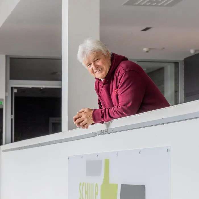 Ein Mann der sich auf eine Mauer lehnt. Darunter steht „Schule mit Weitblick“.