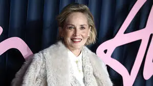 Dieses Bild zeigt die Schauspielerin Sharon Stone. Sie blickt direkt in die Kamera und trägt roten Lippenstift und einen weißen Mantel.
