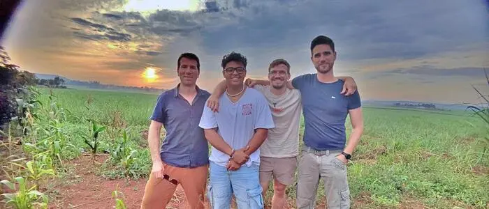 Vier junge Männer stehen in der afrikanischen Savanne, im Hintergrund geht die Sonne unter