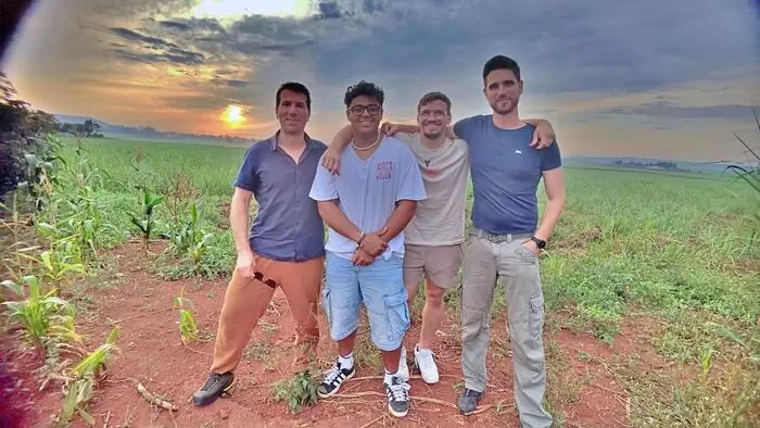 Vier junge Männer stehen in der afrikanischen Savanne, im Hintergrund geht die Sonne unter