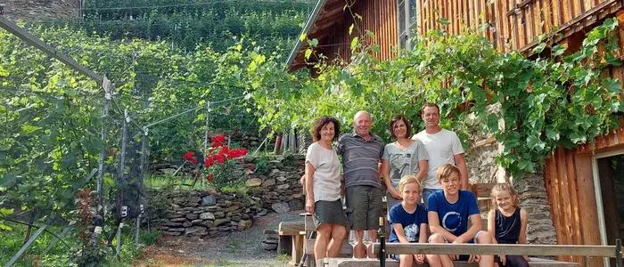 Ein Gruppenfoto einer Familie mit mehreren Generationen darauf. Im Hintergrund ist eine Burg und zahlreiche Weinpflanzen