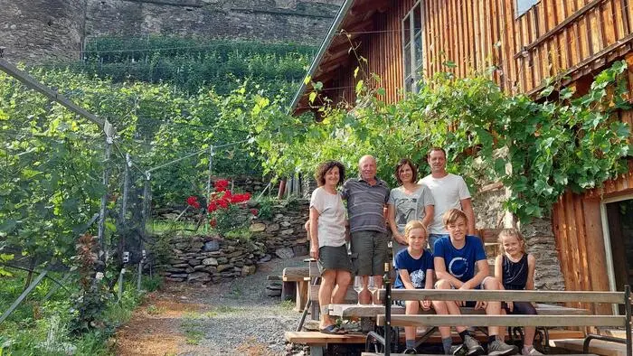 Ein Gruppenfoto einer Familie mit mehreren Generationen darauf. Im Hintergrund ist eine Burg und zahlreiche Weinpflanzen