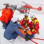Skiretter und ein Verletzter auf der Piste, dahinter ein Rettungshubschrauber | Die ARA Flugrettung im Einsatz