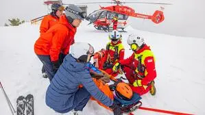 Skiretter und ein Verletzter auf der Piste, dahinter ein Rettungshubschrauber | Die ARA Flugrettung im Einsatz