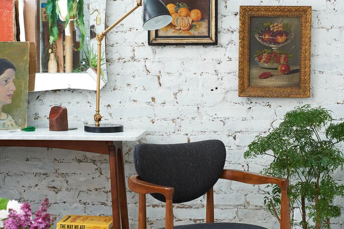 ... gerahmte alte Gemälde auf gestrichenem Backstein zeigen, dass sich Flohmarktschnäppchen bestens für den lässigen Hipster-Stil eignen. Ein Midcentury-Konsolentisch mit Marmorplatte dient als Podest für ein Stilleben aus Bildern und Flohmarkt-Fundstücken.