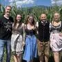 Drei Frauen und zwei Männer in Tracht stehen vor einem Maisfeld und lachen in die Kamera
