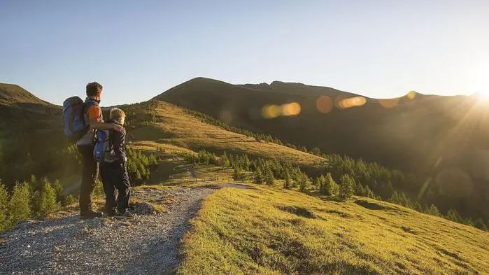 Ein Mann und ein Kind in Wanderausrüstung schauen in den Nockbergen in den Sonnenaufgang.